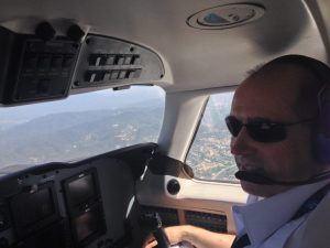Un piloto con gafas de sol vuela hábilmente un Vuelo en avión en Barcelona sobre un impresionante paisaje montañoso cerca de la ciudad, bajo un cielo azul claro. - ForTwo - Planes para parejas