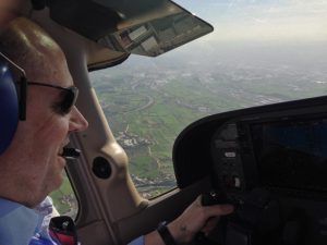 Un piloto vuela en avión en Barcelona, con auriculares y gafas de sol, sobrevolando pintorescos paisajes cerca de Barcelona con campos que se extienden junto a un río sinuoso. - ForTwo - Planes para parejas