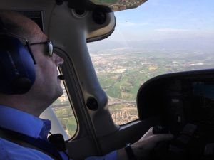Un piloto con auriculares vuela con destreza el Vuelo en avión en Barcelona, sobrevolando impresionantes paisajes con amplios campos y la animada ciudad de Barcelona visible a través de la ventana. - ForTwo - Planes para parejas