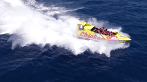 Una lancha rápida amarilla, llamada "Surca las olas a toda velocidad en Chicken Boat en Barcelona", navega por las aguas azules de Barcelona, creando deslumbrantes olas blancas y rocío. - ForTwo - Planes para parejas