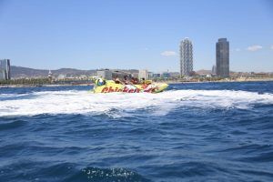 Los pasajeros disfrutan de un vibrante horizonte urbano y de majestuosas montañas mientras el Chicken Boat, una lancha rápida amarilla, navega por las olas de Barcelona. - ForTwo - Planes para parejas