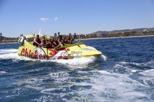 La gente disfruta de la emoción de un paseo en lancha rápida Chicken Boat entre olas vibrantes, con el impresionante paisaje urbano de Barcelona como telón de fondo. - ForTwo - Planes para parejas