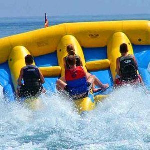 Un Flyfish inflable amarillo remolca a cuatro personas por el brillante mar de Barcelona, creando divertidas salpicaduras a su paso. Vive la emoción con "Salta por los aires sobre el mar practicando el Flyfish en Barcelona". - ForTwo - Planes para parejas