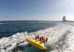Experimenta la emoción de un paseo con Flyfish en un barco inflable amarillo en el océano de Barcelona, con el impresionante horizonte de la ciudad como telón de fondo. - ForTwo - Planes para parejas