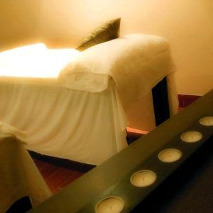 El Circuito en Spa + masaje del Granada Palace incluye una camilla de masaje, iluminación suave y pequeñas velas sobre una superficie oscura, creando un ambiente ideal para la relajación y el rejuvenecimiento. - ForTwo - Planes para parejas