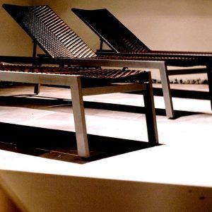 Dos tumbonas con respaldo tejido y estructura de metal en un patio iluminado por el sol, perfectas para relajarse después de disfrutar de un Circuito en Spa + masaje en Granada Palace. - ForTwo - Planes para parejas