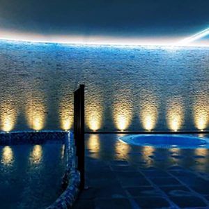 Experimente la relajación definitiva con el Circuito de Spa + Masaje en Granada Palace. Disfrute de un spa con luz tenue, con una pared de piedra iluminada, una piscina resplandeciente y un jacuzzi circular, perfecto para disfrutar de masajes relajantes en este sereno santuario. - ForTwo - Planes para parejas