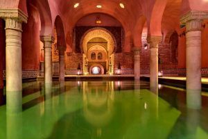 El ornamentado interior de Hammam Al Ándalus Granada Baños Árabes, que recuerda a los históricos baños andaluces, cuenta con elegantes arcos, majestuosos pilares y un sereno estanque verde reflectante. - ForTwo - Planes para parejas