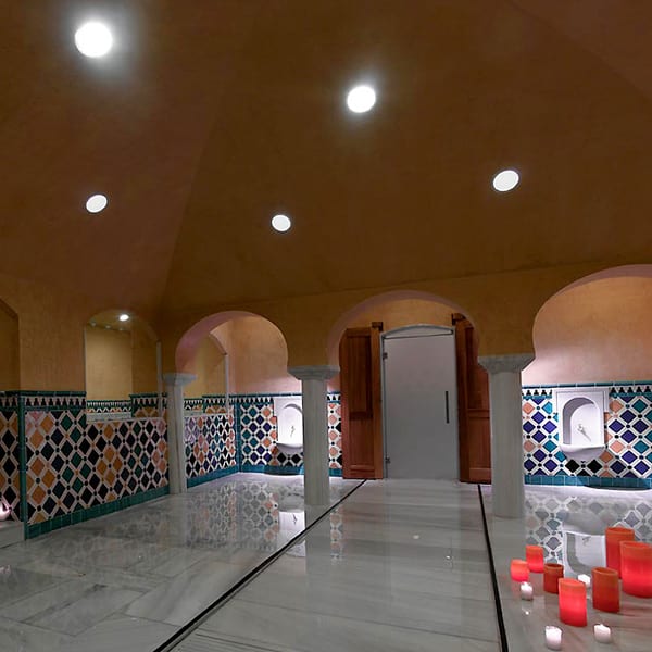 Elegante sala de spa con pisos de mármol, intrincadas paredes de mosaicos inspiradas en los Baños Árabes, luces ambientales en el techo y pasillos iluminados con velas. Ideal para disfrutar de la OFERTA: Circuito en Baños Árabes para 2 con cava, bombones y masaje opcional. - ForTwo - Planes para parejas