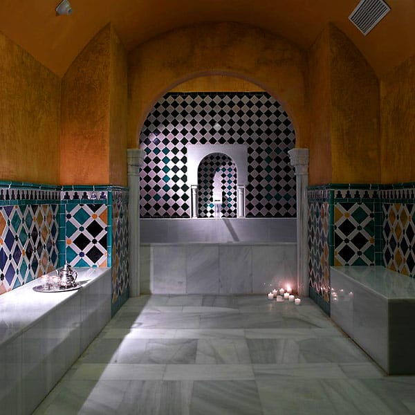El interior de Baños Árabes presume de suelos de mármol, azulejos geométricos, una entrada arqueada y una suave luz de velas que crea un ambiente sereno. Disfrute del "Circuito en Baños Árabes para 2" con cava, bombones y masaje opcional en este acogedor espacio. - ForTwo - Planes para parejas