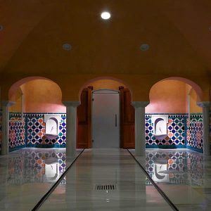 Habitación ornamentada con vibrantes paredes de azulejos y puertas arqueadas, realzada por una cálida iluminación ambiental que crea un ambiente sereno. Perfecta para disfrutar de la OFERTA: Circuito en Baños Árabes para 2 con cava, bombones y masaje opcional sobre su brillante suelo reflectante. - ForTwo - Planes para parejas