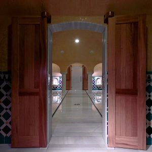 Puertas de madera conducen a un pasillo con arcos y paredes estampadas en una habitación con poca luz, que se asemeja a una OFERTA: Circuito en Baños Árabes para 2 con cava, bombones y masaje opcional. - ForTwo - Planes para parejas