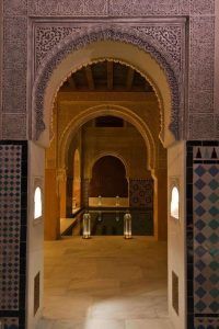 Un arco ornamentado conduce al Baño con masaje de estilo marroquí MIMMA 15 en Hammam Al Ándalus Málaga, donde los azulejos estampados y las linternas crean un ambiente sereno y exótico. - ForTwo - Planes para parejas