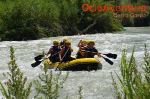 Los aventureros se adentran en las Aguas Bravas del Río Genil en una balsa de color amarillo vibrante, envuelta por un exuberante paisaje verde. - ForTwo - Planes para parejas
