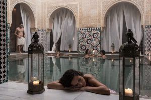 Una mujer se relaja junto a la ornamentada piscina del Hammam Al Ándalus Málaga, disfrutando del agua y de la arquitectura morisca, como parte de la experiencia Exclusivo MIDRA. - ForTwo - Planes para parejas