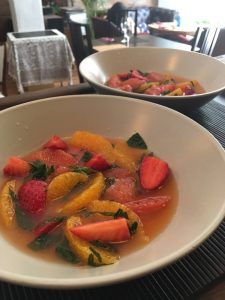 Dos tazones de ensalada de frutas con fresas, rodajas de naranja y hierbas en un caldo ligero descansan elegantemente sobre una bandeja oscura, encarnando los vibrantes sabores de Málaga en el Restaurante La Luz de la Candela - Málaga. - ForTwo - Planes para parejas