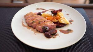 En Restaurante La Luz de la Candela - Málaga, disfrute de pechuga de pato en rodajas con salsa, servida con zanahorias, patatas y remolachas en un plato blanco crujiente. - ForTwo - Planes para parejas