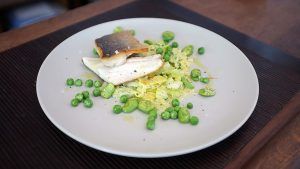 En el Restaurante La Luz de la Candela de Málaga, disfrute de un delicioso filete de pescado a la parrilla sobre guisantes y col rallada, bellamente servido en un plato blanco. - ForTwo - Planes para parejas