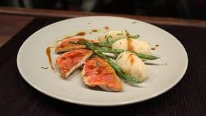 Un plato servido en el Restaurante La Luz de la Candela - Málaga incluye suculentos filetes de pescado, crujientes judías verdes y delicadas quenelles en un plato blanco impecable. - ForTwo - Planes para parejas