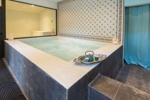 El Ritual Básico con exfoliación en Le Patio Spa ofrece un baño de spa interior con una pared de azulejos decorativos, una bandeja con un juego de té en el borde y un escalón para subir, lo que hace que cada momento sea relajante para su alma. - ForTwo - Planes para parejas