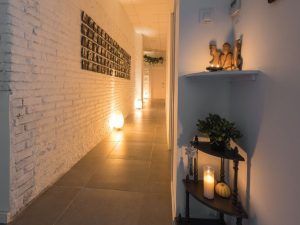 Un acogedor pasillo con iluminación suave, velas, una escultura y una pared de fotos sobre ladrillos texturizados crean un ambiente cálido que recuerda la experiencia del Ritual Básico con exfoliación en Le Patio Spa. - ForTwo - Planes para parejas