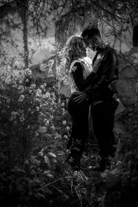 En un jardín sombreado y lleno de flores en Málaga, una pareja comparte un abrazo íntimo entre árboles y una luz suave, capturando perfectamente la esencia de una sesión fotográfica boudoir en pareja Málaga. - ForTwo - Planes para parejas