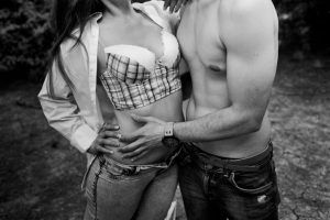 Un hombre y una mujer con ropa informal se abrazan al aire libre, parcialmente desvestidos, revelando sus torsos en esta cautivadora fotografía en blanco y negro, un hermoso momento de una sesión fotográfica boudoir en pareja Málaga. - ForTwo - Planes para parejas