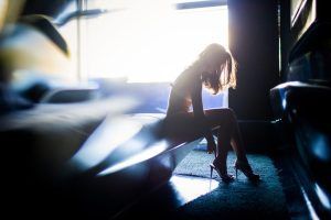 En un tocador suavemente iluminado, una mujer recortada se sienta con gracia, ajustándose los tacones altos durante su "Sesión fotográfica boudoir en pareja Málaga". - ForTwo - Planes para parejas