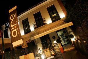 La vista nocturna muestra el ambiente vibrante de Aire Gastrobar - Cocina mediterránea de autor, con un gran cartel de "Aire" coronando la entrada e invitando a los comensales a entrar. - ForTwo - Planes para parejas