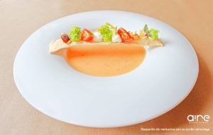 Disfrute de una experiencia culinaria mediterránea en Aire Gastrobar con nuestra cremosa sopa de naranja, servida en un plato blanco y elegantemente adornada con pan crujiente, verduras frescas y vegetales. - ForTwo - Planes para parejas