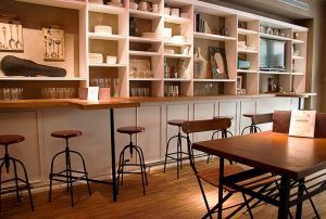 El acogedor interior de la cafetería con taburetes altos, mesas de madera y estantes decorativos que exhiben los platos encarna el encanto del Restaurante La Cocotte Cocina internacional en Málaga. - ForTwo - Planes para parejas