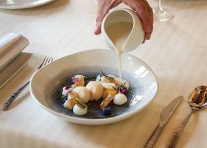 Salsa rociada sobre vieiras con guarniciones vibrantes en un plato blanco en Aire Gastrobar - Cocina mediterránea de autor, que ejemplifica la cocina mediterránea en una elegante mesa de comedor. - ForTwo - Planes para parejas