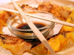 Un plato de empanadillas fritas doradas con salsa de soja en un bol de cristal y palillos de madera es la manera perfecta de saborear el sabor de la cocina internacional en Restaurante La Cocotte Cocina internacional en Málaga, que encarna la vibrante escena culinaria de la ciudad. - ForTwo - Planes para parejas