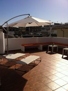 La soleada terraza en la azotea de Málaga cuenta con tumbonas, una mesa, bancos y una gran sombrilla blanca, ideal para relajarse después de disfrutar del Baño sencillo en el Hammam Spa de Málaga. - ForTwo - Planes para parejas
