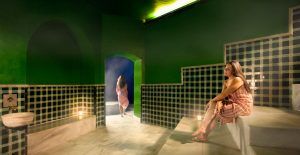 Dos mujeres en el Hammam Spa de Málaga: una sentada en una cornisa, la otra caminando con gracia por un arco, evocando una atmósfera de serenidad. Producto: Baño sencillo en el Hammam Spa de Málaga. - ForTwo - Planes para parejas