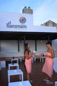 Dos personas vestidas con toallas a rayas conversan y sostienen tazas en la tranquila zona al aire libre de El Hammam Open Space & Spa de Málaga, disfrutando de un Baño sencillo en el Hammam Spa de Málaga. - ForTwo - Planes para parejas