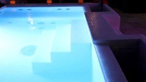 The Magic Experience Urban Spa 1850 Barcelona cuenta con una piscina iluminada con un tono azul brillante, escalones, un borde de azulejos y pequeñas luces naranjas: una verdadera joya escondida en la ciudad. - ForTwo - Planes para parejas
