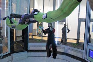 Dos personas con trajes de vuelo experimentan la emoción del paracaidismo en túnel de viento en Windobona Indoor Skydiving en Madrid, elevándose sin esfuerzo en un túnel de viento vertical con la guía experta de un instructor. - ForTwo - Planes para parejas