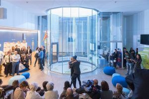 En un ambiente moderno y elegante, la gente se reúne alrededor del cristal “Paracaidismo en túnel de viento Windobona Indoor Skydiving en Madrid” para presenciar cómo dos personas viven la emocionante experiencia del paracaidismo en interiores. - ForTwo - Planes para parejas