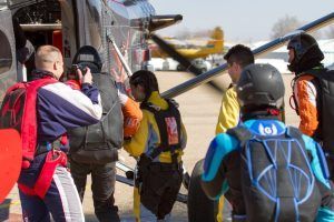 Paracaidistas vestidos con coloridos monos y cascos suben a un avión en un día soleado, ansiosos por disfrutar de un emocionante salto en paracaídas con Skydive Madrid sobre los vibrantes paisajes de Madrid. - ForTwo - Planes para parejas