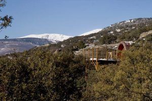 Una Cabaña en el árbol para ir en pareja en MonteHoliday Madrid se encuentra en lo alto de una plataforma entre frondosos árboles con montañas cubiertas de nieve como impresionante telón de fondo, ideal para parejas que buscan tranquilidad y belleza natural. - ForTwo - Planes para parejas