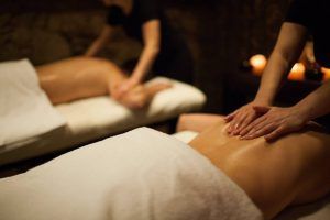Dos personas disfrutan de masajes relajantes en camillas rodeadas de iluminación tenue y velas en un ambiente sereno, realzado por tratamientos de vinoterapia en Vinoterapia en el spa urbano Ambrosia en el corazón de Barcelona. - ForTwo - Planes para parejas