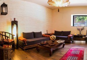 Un acogedor salón con dos sofás, muebles de madera, cojines de colores y una iluminación cálida que evoca el encanto de la Vinoterapia en el spa urbano Ambrosia de Barcelona. - ForTwo - Planes para parejas