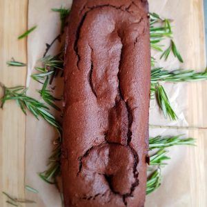 Sobre papel vegetal reposa un bizcocho de chocolate, adornado con ramitas de romero, un capricho ideal para el "Brunch de comida local en MAAI Barcelona". - ForTwo - Planes para parejas