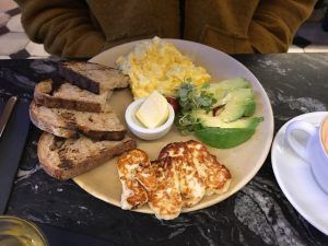 En Enkel, un local de gastro-brunch en Barcelona, una mesa de mármol exhibe el "Gastro-brunch en Enkel Barcelona" con huevos revueltos, halloumi a la parrilla, tostadas, aguacate, ensalada y mantequilla. - ForTwo - Planes para parejas