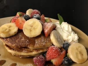 Disfruta de un delicioso brunch gastronómico en Enkel Barcelona con panqueques adornados con plátanos, fresas, arándanos, frambuesas, azúcar glas y crema batida. - ForTwo - Planes para parejas