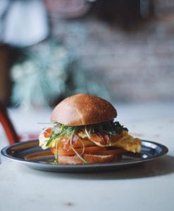 En el restaurante Brunch en Picnic de Barcelona, disfruta de un sándwich de brunch gourmet con aguacate, verduras y una tortilla esponjosa en un pan, servido elegantemente en un plato de metal. - ForTwo - Planes para parejas