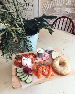 El “Brunch en Picnic” del Restaurante Barcelona ofrece un delicioso combo: bagel con salmón ahumado, queso crema, tomates, pepinos, rábanos y hierbas sobre una tabla de madera, ideal para un brunch o un picnic. - ForTwo - Planes para parejas