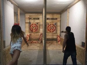En El Hachazo de Madrid, dos personas lanzan hachas a objetivos de madera dentro de un recinto de red en la emocionante experiencia conocida como "Tiro con hacha en Madrid con El Hachazo", perfecta para probar la puntería y la precisión. - ForTwo - Planes para parejas