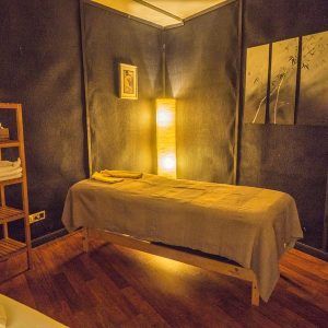 Una habitación poco iluminada con una mesa de masajes, una lámpara brillante y arte en la pared, todo parte de la experiencia "Spa y masaje a lo japonés + menú de tapas en Madrid". - ForTwo - Planes para parejas